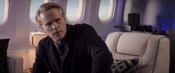 Movie still from “Operation Fortune: Ruse de Guerre” (2023), directed by Guy Ritchie – A man sitting on an airplane with his hand on his shoulder; Medium shot, Over the shoulder angle