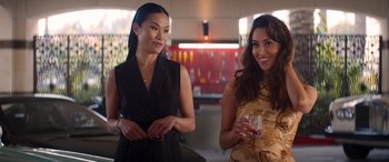 Movie still from “Operation Fortune: Ruse de Guerre” (2023), directed by Guy Ritchie – Two women standing next to each other holding drinks; Medium shot, Over the shoulder angle