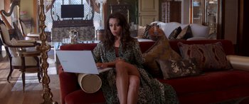 Movie still from “Operation Fortune: Ruse de Guerre” (2023), directed by Guy Ritchie – A woman sitting on top of a red couch using a laptop computer; Medium shot, High angle