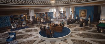 Movie still from “Operation Fortune: Ruse de Guerre” (2023), directed by Guy Ritchie – A person sitting at a desk in a room; Extreme Wide shot, High angle