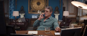 Movie still from “Operation Fortune: Ruse de Guerre” (2023), directed by Guy Ritchie – A man sitting at a table talking on a cell phone; Medium shot, Low angle