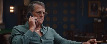 Movie still from “Operation Fortune: Ruse de Guerre” (2023), directed by Guy Ritchie – An older man wearing glasses talking on a cell phone; Close Up shot, Low angle
