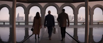 Movie still from “Operation Fortune: Ruse de Guerre” (2023), directed by Guy Ritchie – A group of three people walking on a walkway; Wide shot, Low angle