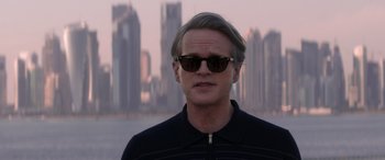 Movie still from “Operation Fortune: Ruse de Guerre” (2023), directed by Guy Ritchie – A man wearing sunglasses standing in front of a city skyline; Close Up shot, Over the shoulder angle