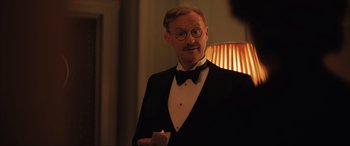 Movie still from “Operation Mincemeat” (2021), directed by John Madden – A man in a tuxedo holding a candle in his hand; Medium shot, Over the shoulder angle