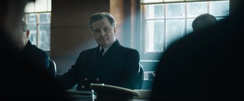 Movie still from “Operation Mincemeat” (2021), directed by John Madden – A man sitting at a table in a room; Medium shot, Over the shoulder angle