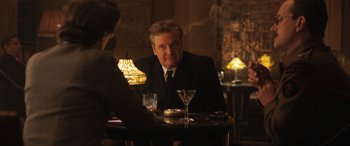 Movie still from “Operation Mincemeat” (2021), directed by John Madden – A man sitting at a table with a glass of wine in front of him; Medium shot, Over the shoulder angle