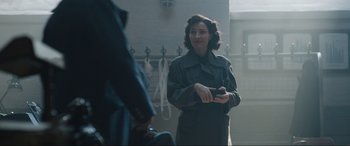 Movie still from “Operation Mincemeat” (2021), directed by John Madden – A woman holding a cell phone while standing in a room; Medium shot, Over the shoulder angle