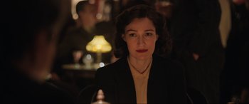 Movie still from “Operation Mincemeat” (2021), directed by John Madden – A woman in a black jacket is sitting at a table; Close Up shot, Over the shoulder angle