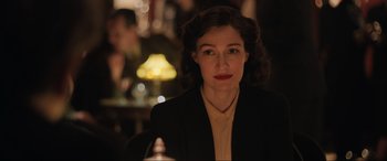 Movie still from “Operation Mincemeat” (2021), directed by John Madden – A woman in a black jacket is sitting at a table in front of a lamp; Close Up shot, Over the shoulder angle