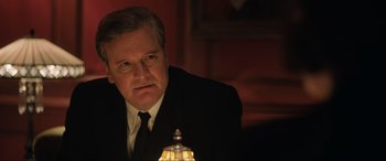 Movie still from “Operation Mincemeat” (2021), directed by John Madden – A man wearing a suit and tie sitting in front of a lamp; Close Up shot, Over the shoulder angle