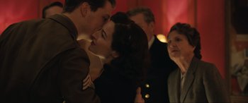 Movie still from “Operation Mincemeat” (2021), directed by John Madden – A man and a woman kissing in front of a group of people; Medium shot, Over the shoulder angle