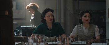Movie still from “Operation Mincemeat” (2021), directed by John Madden – A woman sitting at a dinner table with other people around it; Medium shot, Over the shoulder angle