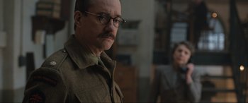 Movie still from “Operation Mincemeat” (2021), directed by John Madden – An older man wearing glasses and wearing a jacket; Close Up shot, Over the shoulder angle