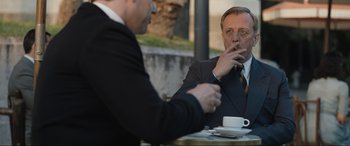 Movie still from “Operation Mincemeat” (2021), directed by John Madden – Two businessmen are sitting at a table and one of them is smoking a cigarette; Medium shot, Over the shoulder angle
