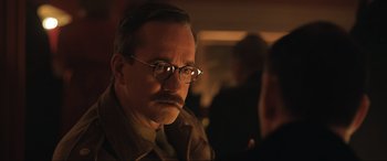 Movie still from “Operation Mincemeat” (2021), directed by John Madden – A man with a mustache wearing glasses and a brown jacket; Close Up shot, Over the shoulder angle