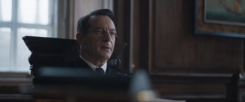 Movie still from “Operation Mincemeat” (2021), directed by John Madden – A man in a uniform sitting in front of a wooden desk; Close Up shot, Over the shoulder angle