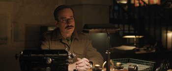 Movie still from “Operation Mincemeat” (2021), directed by John Madden – A man sitting at a table in front of a lamp; Medium shot, Low angle