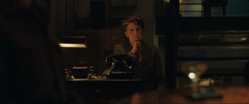 Movie still from “Operation Mincemeat” (2021), directed by John Madden – A woman sitting at a desk in a dark room; Medium shot, Low angle