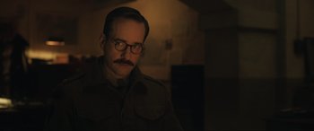 Movie still from “Operation Mincemeat” (2021), directed by John Madden – A man with a mustache wearing glasses and a military uniform; Close Up shot, Low angle