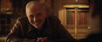 Movie still from “Operation Mincemeat” (2021), directed by John Madden – An older man with white hair smiling for the camera; Close Up shot, Low angle