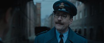 Movie still from “Operation Mincemeat” (2021), directed by John Madden – A man wearing a uniform and a hat and glasses; Close Up shot, Low angle