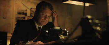 Movie still from “Operation Mincemeat” (2021), directed by John Madden – A man sitting at a table in a room; Close Up shot, Low angle