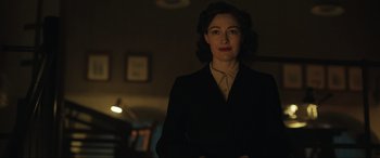 Movie still from “Operation Mincemeat” (2021), directed by John Madden – A woman standing in a dark room wearing a suit and tie; Medium shot, Over the shoulder angle