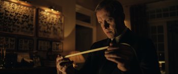 Movie still from “Operation Mincemeat” (2021), directed by John Madden – A man in a suit and tie holding a wooden stick; Close Up shot, Low angle