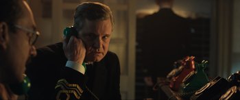 Movie still from “Operation Mincemeat” (2021), directed by John Madden – A man talking on a phone while wearing a suit; Close Up shot, Over the shoulder angle