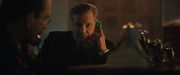 Movie still from “Operation Mincemeat” (2021), directed by John Madden – A man in a black suit is talking on a phone; Close Up shot, Low angle