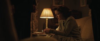 Movie still from “Operation Mincemeat” (2021), directed by John Madden – A woman sitting on a chair in a room with a lamp; Medium shot, High angle
