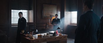 Movie still from “Operation Mincemeat” (2021), directed by John Madden – A man in a suit standing in front of a desk; Wide shot, Low angle