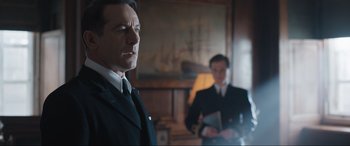 Movie still from “Operation Mincemeat” (2021), directed by John Madden – A man in a suit and tie standing next to another man in a suit and tie; Medium shot, Low angle