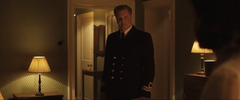 Movie still from “Operation Mincemeat” (2021), directed by John Madden – A man in a uniform standing in a dark room; Medium shot, Low angle