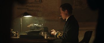 Movie still from “Operation Mincemeat” (2021), directed by John Madden – A man sitting at a table smoking a cigarette; Medium shot, Low angle