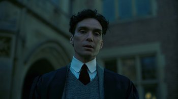 Movie still from “Oppenheimer” (2023), directed by Christopher Nolan – A man in a suit and tie standing in front of a building; Close Up shot, Low angle