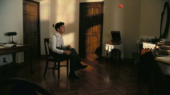 Movie still from “Oppenheimer” (2023), directed by Christopher Nolan – A man sitting on a chair in a living room; Wide shot, High angle