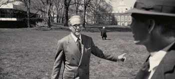 An older man in a suit and tie is throwing a frisbee