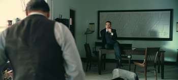Movie still from “Oppenheimer” (2023), directed by Christopher Nolan – A man sitting on a chair in a room; Medium shot, Over the shoulder angle