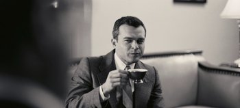 Movie still from “Oppenheimer” (2023), directed by Christopher Nolan – A black and white photo of a man holding a glass of wine; Close Up shot, Low angle