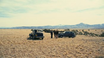 Movie still from “Oppenheimer” (2023), directed by Christopher Nolan – A couple of cars parked on top of a grass covered field; Extreme Wide shot, High angle