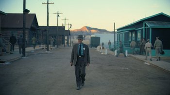 Movie still from “Oppenheimer” (2023), directed by Christopher Nolan – A man in a suit and tie walking down a street; Wide shot, Low angle