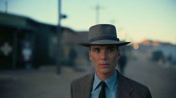 Movie still from “Oppenheimer” (2023), directed by Christopher Nolan – A man wearing a suit and a hat is standing in the street; Close Up shot, Low angle