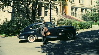Movie still from “Oppenheimer” (2023), directed by Christopher Nolan – A man standing next to an antique car; Wide shot, High angle