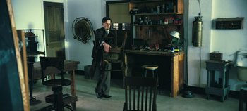 Movie still from “Oppenheimer” (2023), directed by Christopher Nolan – A man holding a chair in a room filled with furniture; Wide shot, High angle