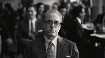 Movie still from “Oppenheimer” (2023), directed by Christopher Nolan – An older man wearing a suit and tie in front of a group of people; Close Up shot, Low angle