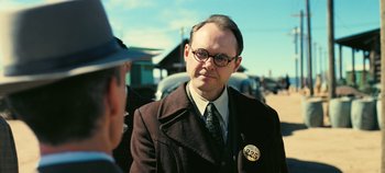 Movie still from “Oppenheimer” (2023), directed by Christopher Nolan – A man in a suit and tie with a badge on his lapel; Close Up shot, Over the shoulder angle