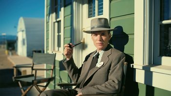 Movie still from “Oppenheimer” (2023), directed by Christopher Nolan – A man in a suit and a hat smoking a pipe; Medium shot, High angle