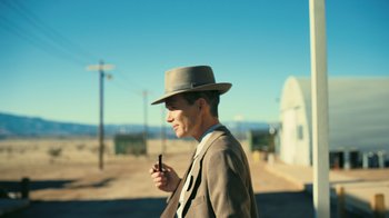 Movie still from “Oppenheimer” (2023), directed by Christopher Nolan – A man wearing a suit and a hat smoking a cigarette; Medium shot, Low angle